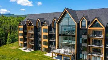 A modern multi-story building with balconies, large windows, and a grassy area in front.