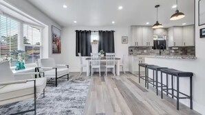A modern kitchen with white cabinets, a dining area with a white table and chairs, and a bar area with stools. - Cozy Master King suite- play room- hot tub (Denver)