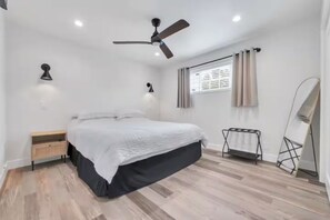 A bedroom with a bed, a ceiling fan, a window with curtains, a bedside table, and a mirror. - Cozy Master King suite- play room- hot tub (Denver)
