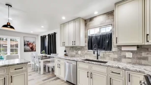 A modern kitchen with white cabinetry, a granite countertop, and a large window with black curtains. - Cozy Master King suite- play room- hot tub (Denver)