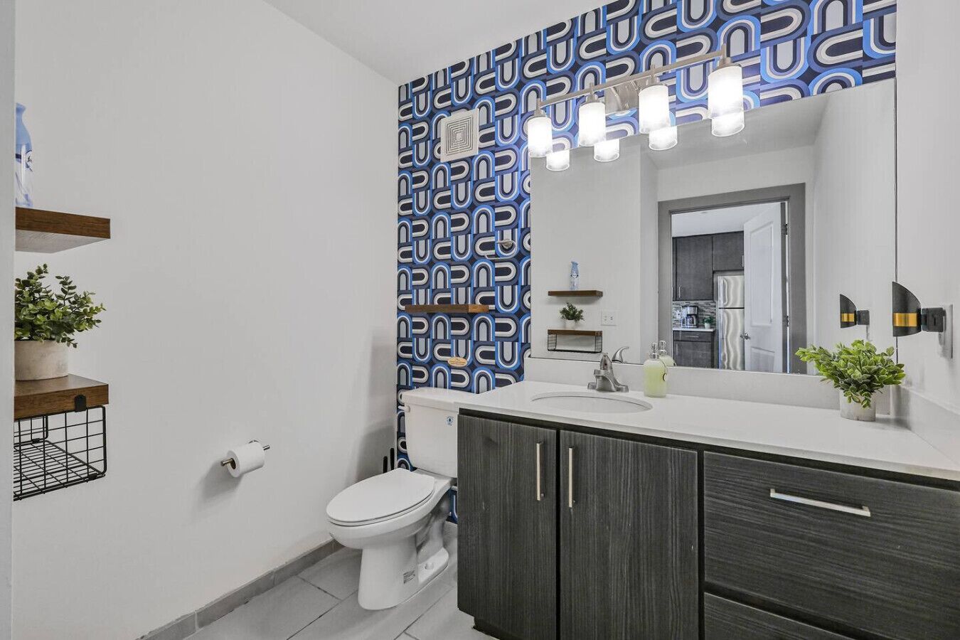 Een moderne badkamer met een patroon op de muur, een toilet, een wastafelmeubel met spiegel en een wastafel.