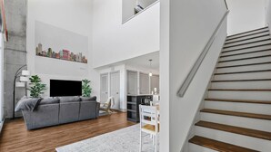 A modern living room with a grey sofa, a flat-screen TV, and a cityscape artwork on the wall. - *NEW* Lux Loft V2 (Close to Vandy!) (Nashville)