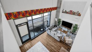 A modern living room with a large window, a gray sofa, a TV, and a cityscape mural on the wall. - *NEW* Lux Loft V2 (Close to Vandy!) (Nashville)