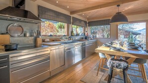 A modern kitchen with stainless steel appliances, a large island, and a dining area with a view of the outdoors. - Chalet du Mont Charvin - Welkeys (Praz-sur-Arly)