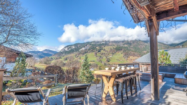 A wooden deck with a table and chairs, overlooking a mountainous landscape. - Chalet du Mont Charvin - Welkeys (Praz-sur-Arly)