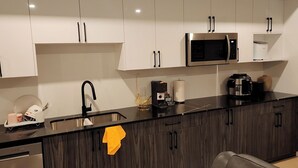 Una cocina moderna con armarios blancos, encimera negra, pileta de acero inoxidable, microondas, cafetera y refrigerador.