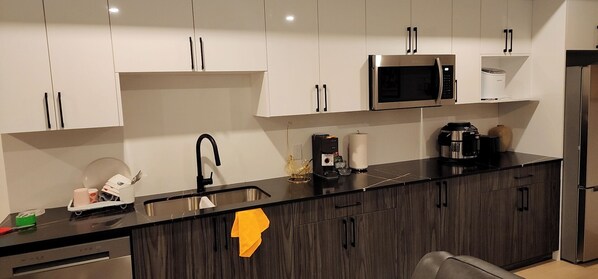 Eine moderne Küche mit weißen Schränken, einer schwarzen Arbeitsplatte, einer Edelstahlspüle, einer Mikrowelle, einer Kaffeemaschine und einem Kühlschrank.