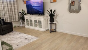 Una sala de estar con televisor de pantalla plana, armarios blancos, una planta en maceta y un espejo en la pared.