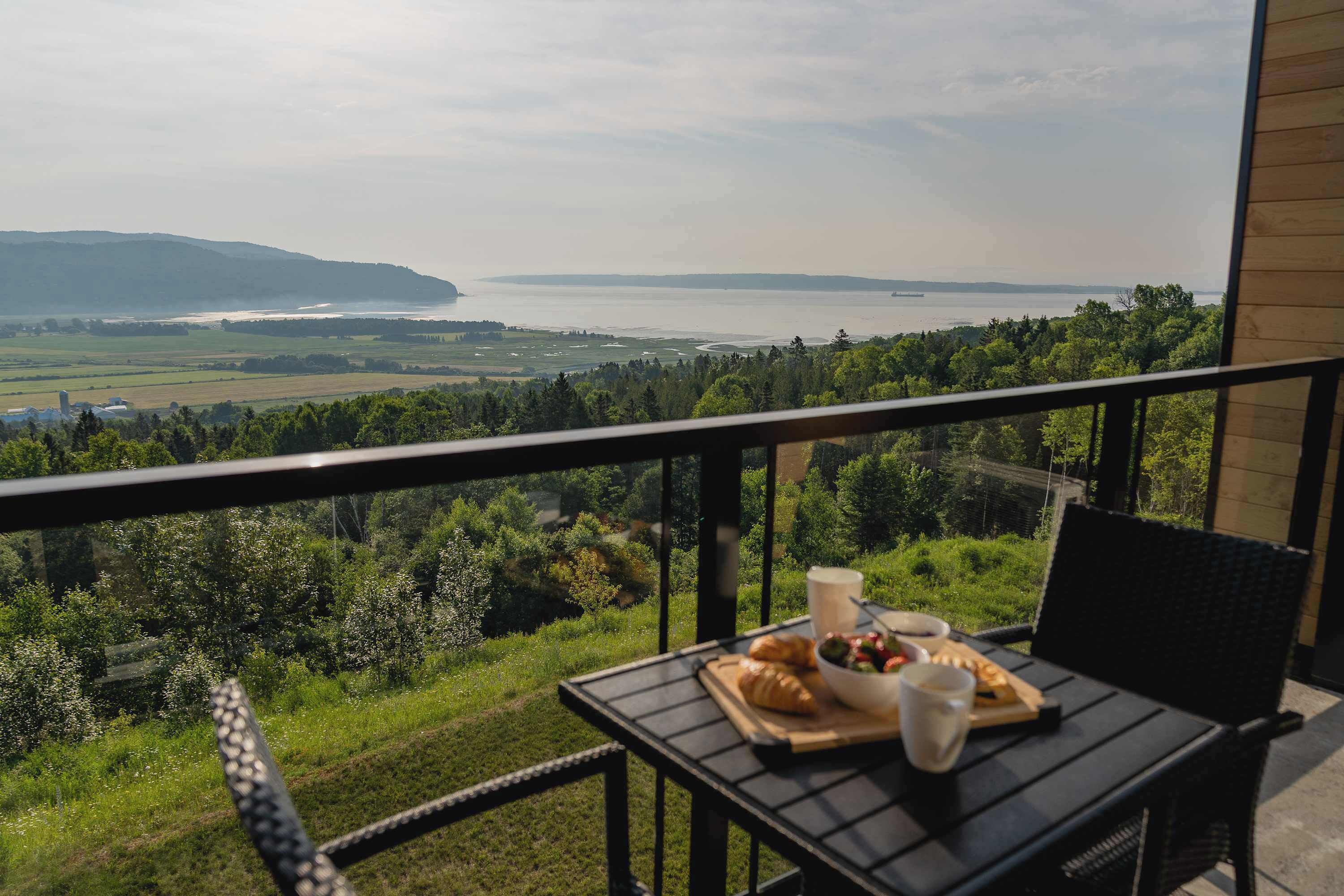 A balcony with a table set for breakfast overlooking a scenic view of a body of water and distant land.