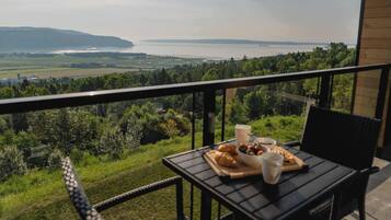 A balcony with a table set for breakfast overlooking a scenic view of a body of water and distant land.