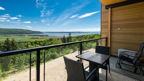 Een balkon met een tafel en stoelen, met uitzicht op een prachtig meer en bos.