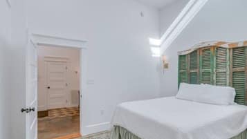 Un dormitorio con cama, una puerta y una ventana con contraventanas.