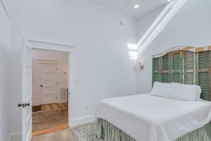 Een slaapkamer met een bed, een deur en een raam met luiken.