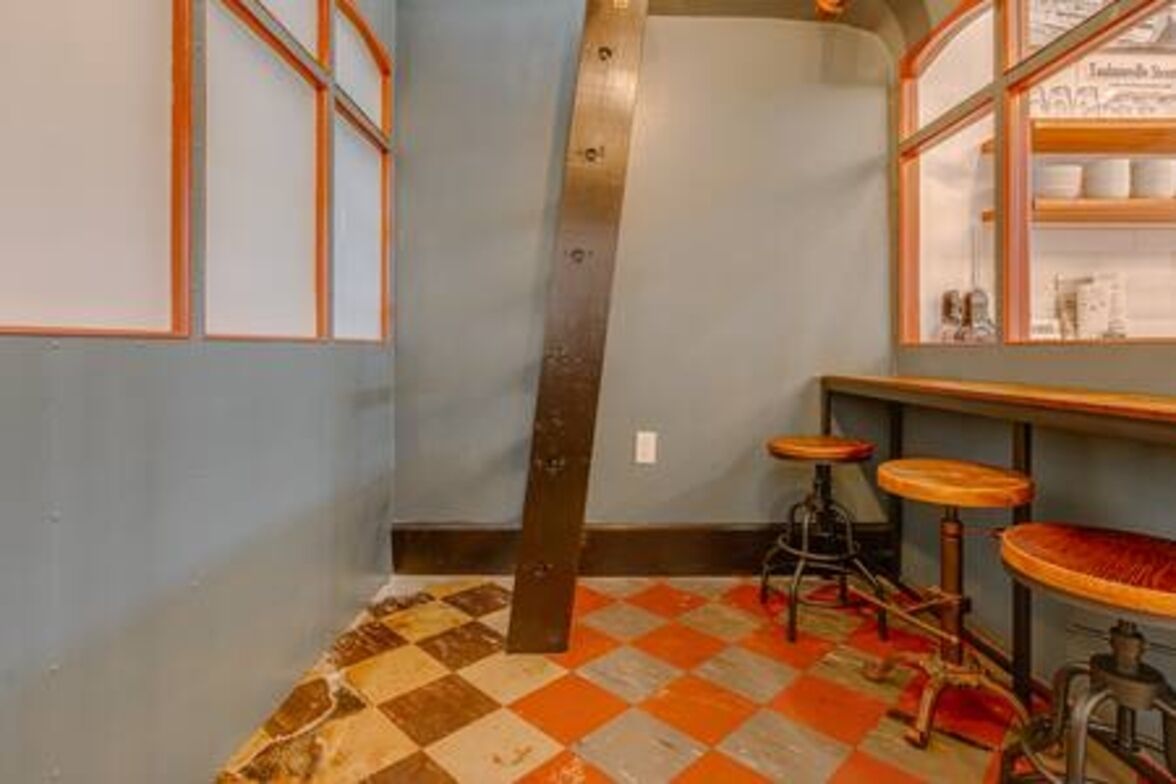 A room with a checkered floor, a bar area with stools, and a window with shelves.