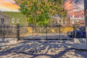 A gated driveway with a tree and buildings in the background.