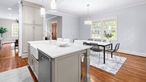 Una cocina moderna con armarios blancos, una isla central, iluminaci ón colgante y una zona de comedor con mesa y sillas.
