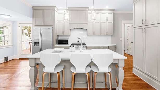 Cocina moderna con armarios blancos, una isla central con taburetes altos, electrodomésticos de acero inoxidable e iluminación colgante.
