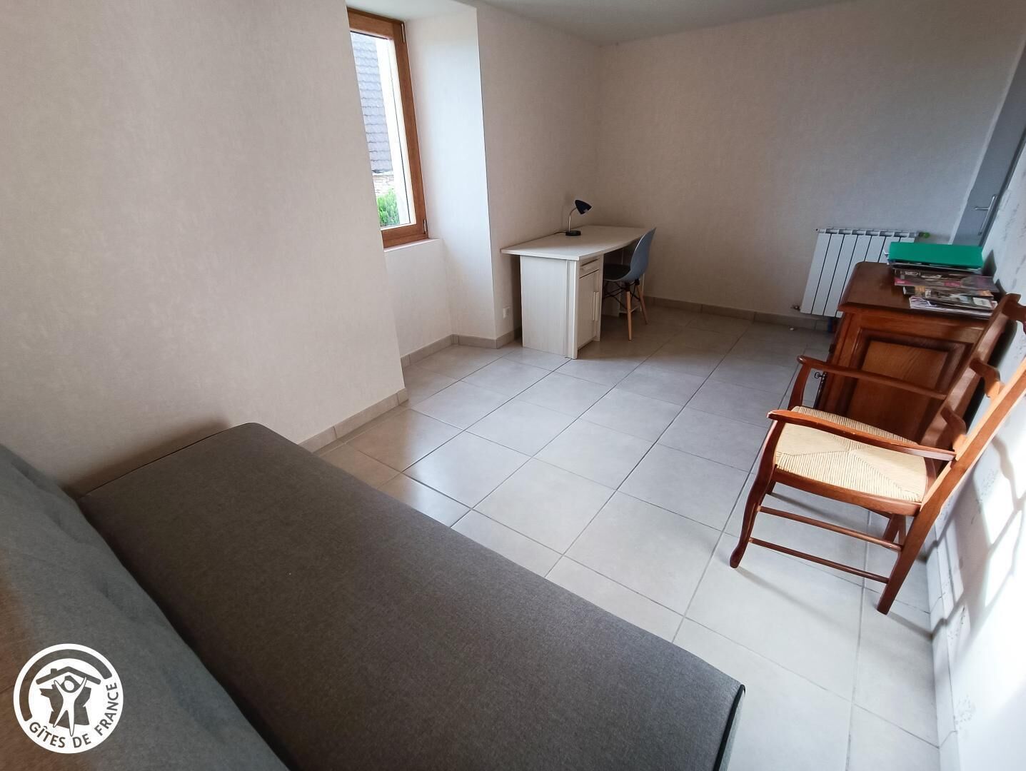 A small, sparsely furnished room with a bed, a desk, and a chair.