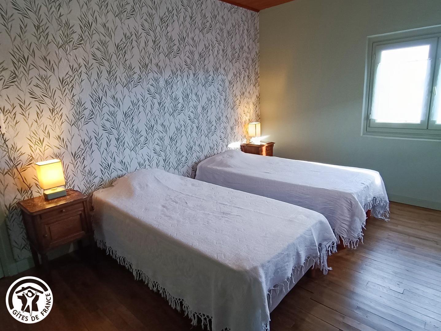 Ein Zimmer mit zwei Betten, Holzböden und einem gemusterten Wandteppich.