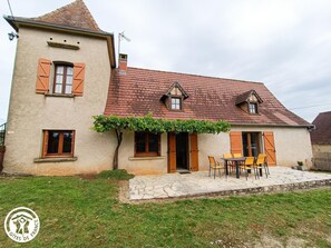 Ein zweistöckiges Haus mit einer Steinterrasse, Holzläden und einem kleinen Garten.