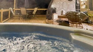 Un espace avec un bain à remous, doté d’une structure en forme de dôme transparent, de guirlandes lumineuses et d’une terrasse en bois.