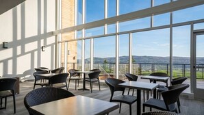 A spacious indoor area with large windows, tables, chairs, and a view of the landscape.
