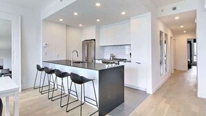 A modern kitchen with a central island, bar stools, stainless steel appliances, and a minimalist design.