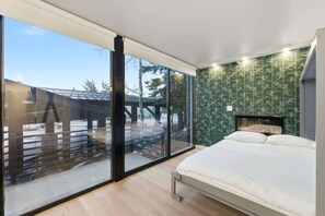 Ein modernes Schlafzimmer mit einem großen Schiebeglasfenster, einem Bett und einem Kamin.