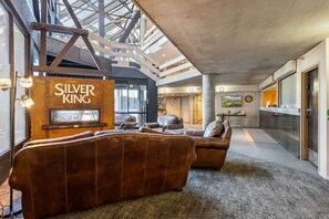 Ein modernes Interieur mit einer großen Sofagarnitur, einem Schild mit der Aufschrift 'SILVER KING' und einem Blick zum Himmel durch eine hohe Decke.
