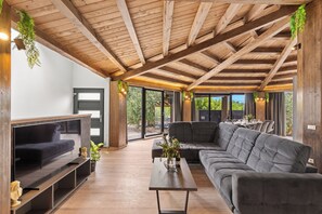 Un salon moderne avec un plafond en bois, un grand canapé d’angle gris, un téléviseur à écran plat et un coin repas avec une table et des chaises.