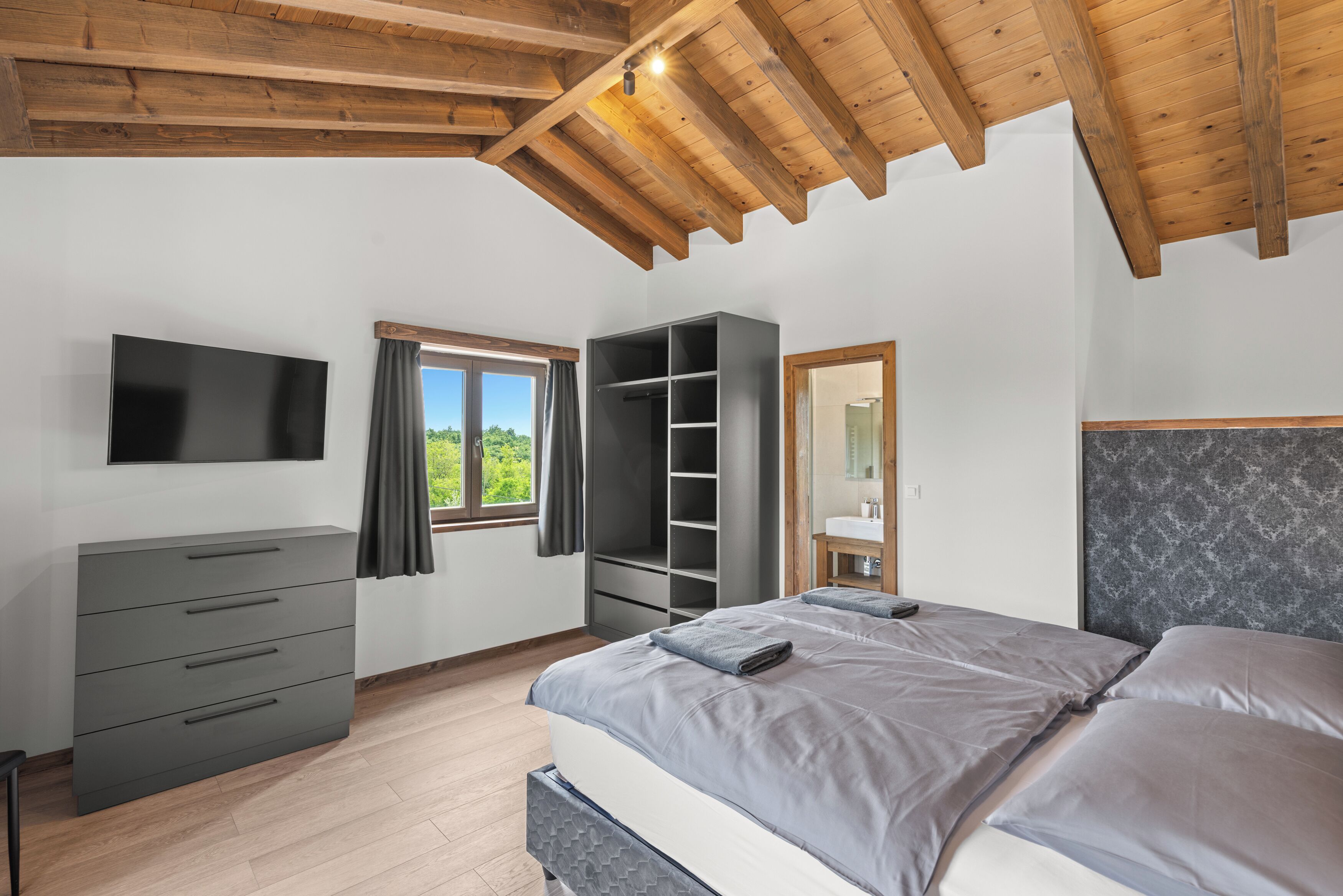 Une chambre à coucher avec un lit, une armoire, une télévision et une fenêtre avec des rideaux.
