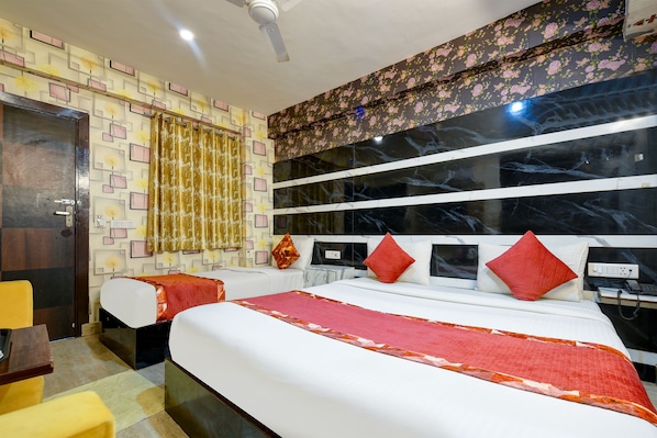 A hotel room with two beds, a desk, a chair, a wardrobe, and a bathroom with a mirror and sink. - Hotel Edisson View (New Delhi)