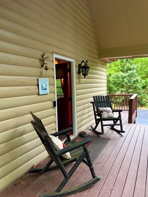 A wooden cabin with a porch, a rocking chair, a lounge chair, a welcome sign, and a lantern.