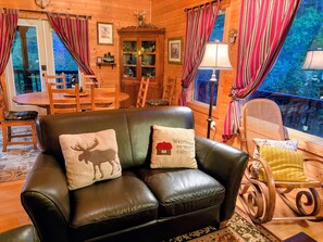 A cozy cabin interior with a leather couch, wooden dining table, and a rocking chair. - One of a kind  secluded Private Cabin -  Cozy 3-bedroom 2acres minutes to Helen (Sautee Nacoochee)