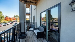 Un balcon doté d’une terrasse en bois, de meubles d’extérieur et offrant une vue sur un parking et des arbres.