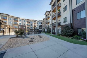 A multi-story residential building with balconies, a paved courtyard, and a small garden area. - 2nd Floor Apt + Amenities - South Springfield (Springfield)