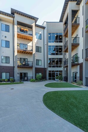 A multi-story residential building with balconies, a central courtyard, and a well-maintained lawn.