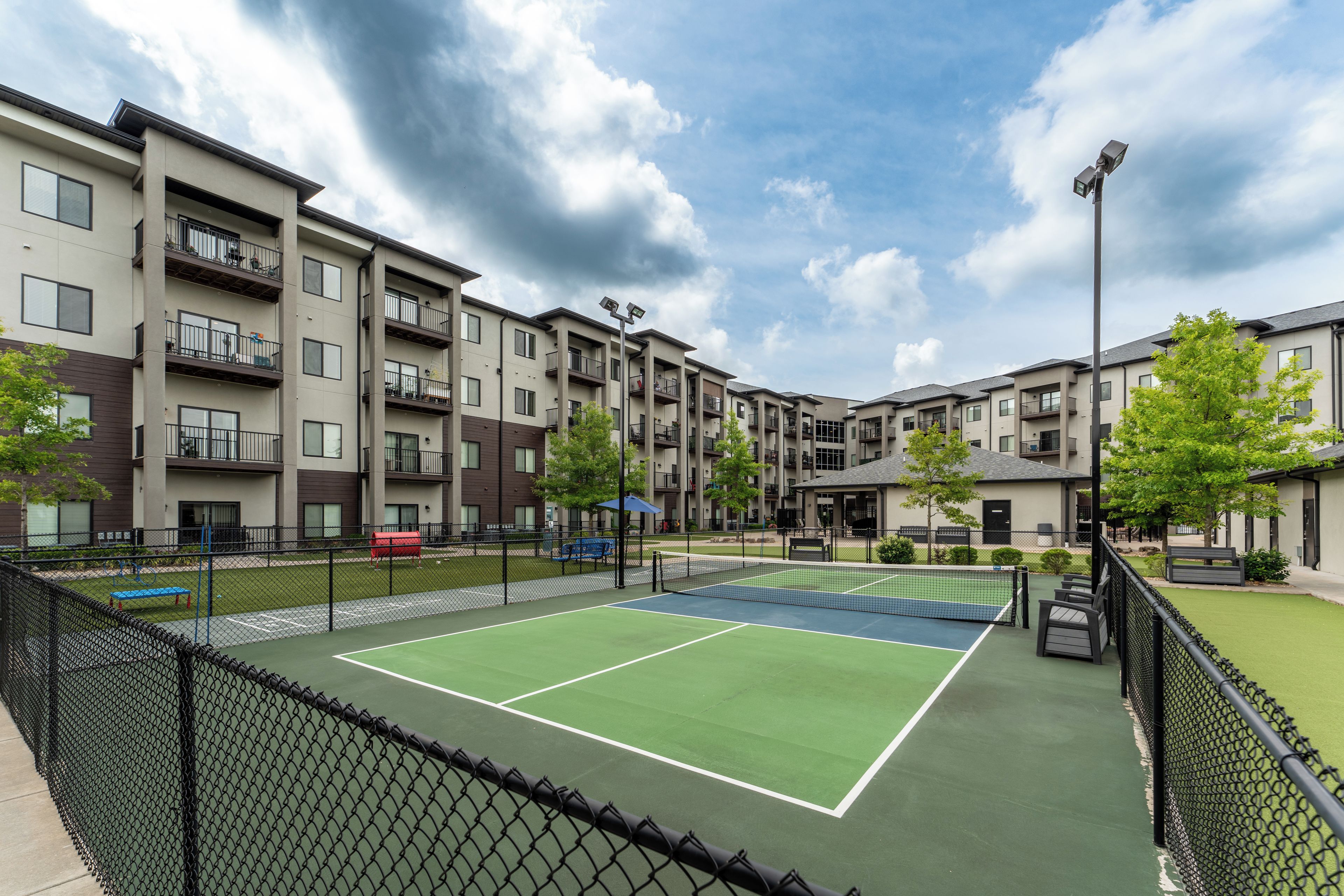 Ein Tennisplatz, umgeben von Mehrfamilienhäusern mit Balkonen.