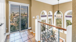 Un balcó ample amb una porta corredissa de vidre, una escala de fusta amb barana de metall decorativa i vista cap a cases properes.