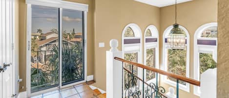 A spacious balcony with a sliding glass door, a wooden staircase with ornate metal railings, and a view of neighboring houses.