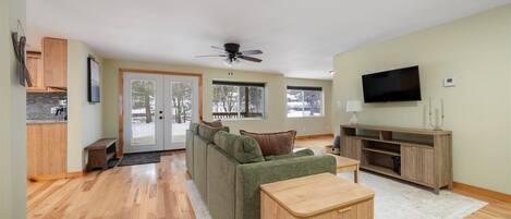 A spacious living room with a green sofa, wooden coffee table, and a TV on a wooden stand.
