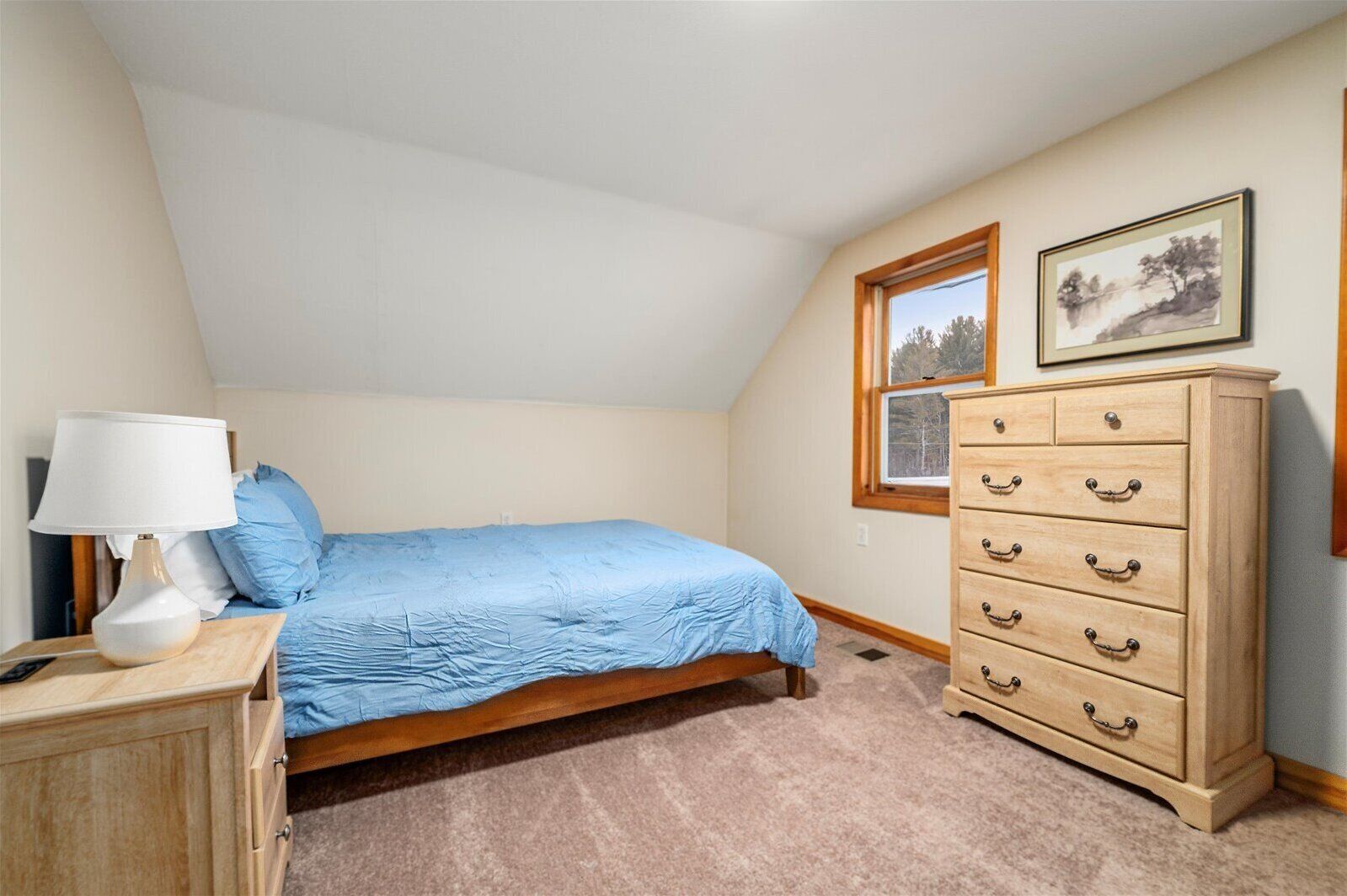 A bedroom with a single bed, a dresser, a lamp, and two framed pictures on the wall.
