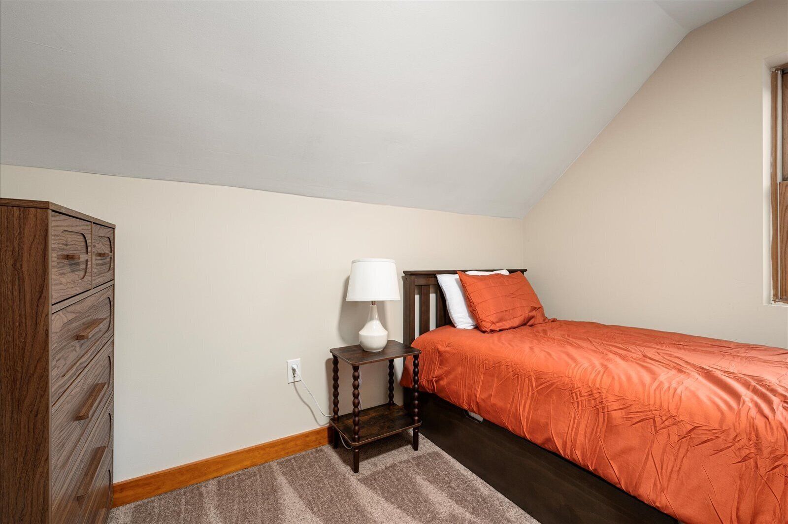 A bedroom with a bed, a nightstand, a lamp, and a wooden wardrobe.