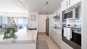 A modern kitchen with stainless steel appliances, a central island, and a view of the sea. - Delightful 2 bedroom condo Encantame Towers Verano 705 (Puerto Peñasco)