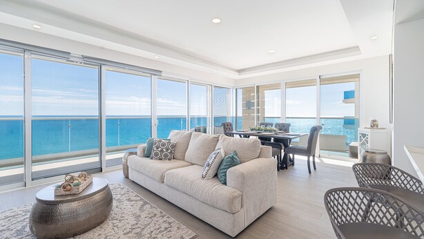 A spacious balcony with a view of the sea, a modern living area with a sofa and chairs, and a dining table set for two. - Delightful 2 bedroom condo Encantame Towers Verano 705 (Puerto Peñasco)
