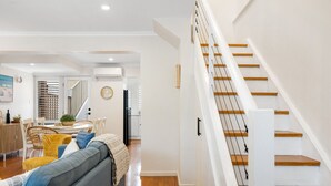 Een moderne woonkamer met een grijze bank, houten vloeren en een trap met witte leuningen.