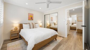 Een moderne slaapkamer met een houten bed, bedlampen, een plafondventilator en een grote spiegel.