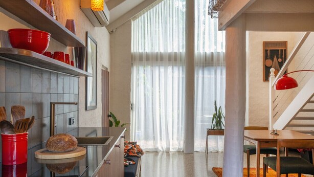 Een moderne keuken met een inbouwoven, een eethoek met een trap, en een groot raam met dunne gordijnen.