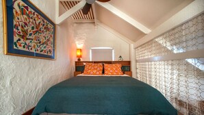 Een slaapkamer met een bed, nachtkastje, lamp en een schilderij aan de muur.