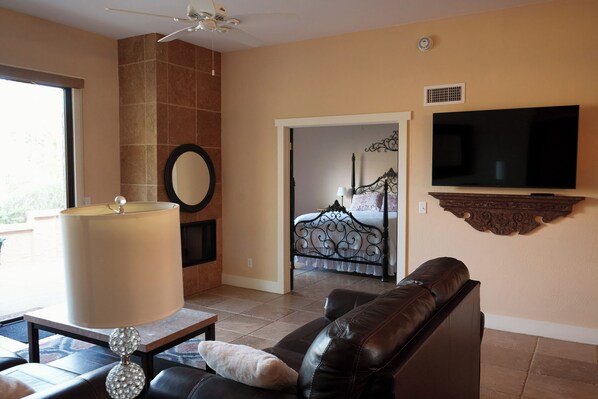A living room with a leather sofa, a TV mounted on the wall, a large window, and a door leading to a bedroom. - Carefree Paradise (Carefree)